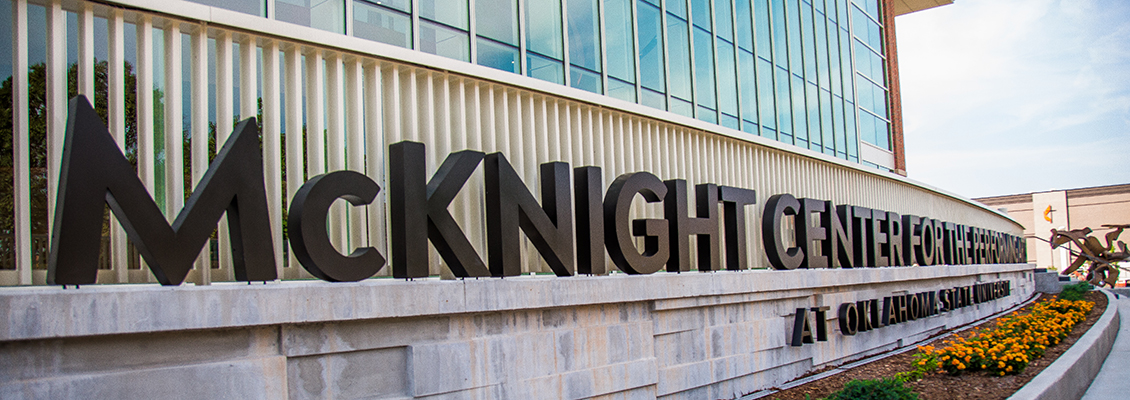 An image of the front flowerbed at The McKnight Center. Large letters line the edge of the flower bed and read "McKnight Center for the performing arts at Oklahoma State University." There are golden yellow marigold flowers in the flower bed.